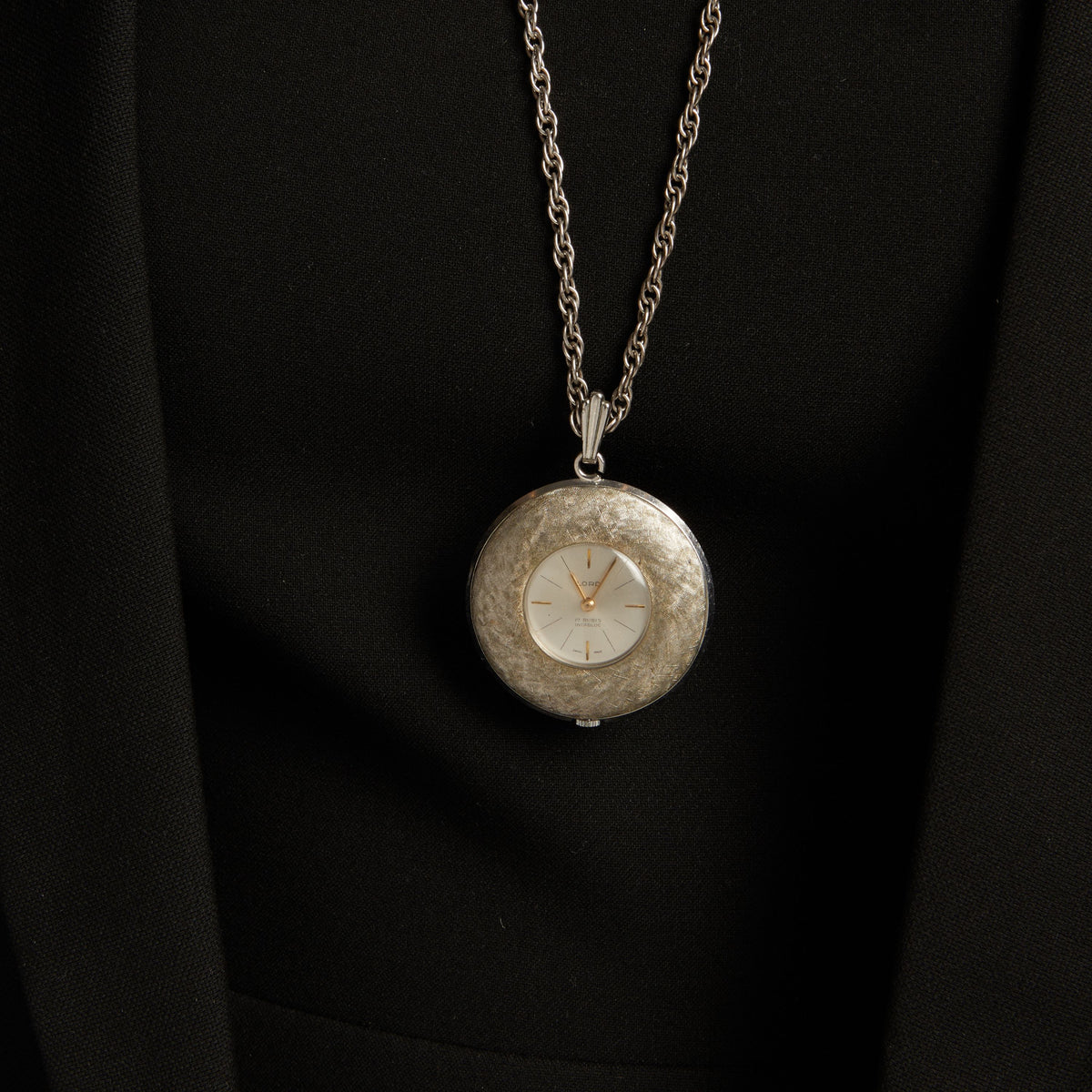 Close up of a woman wearing a large watch pendant necklace on neutral background.