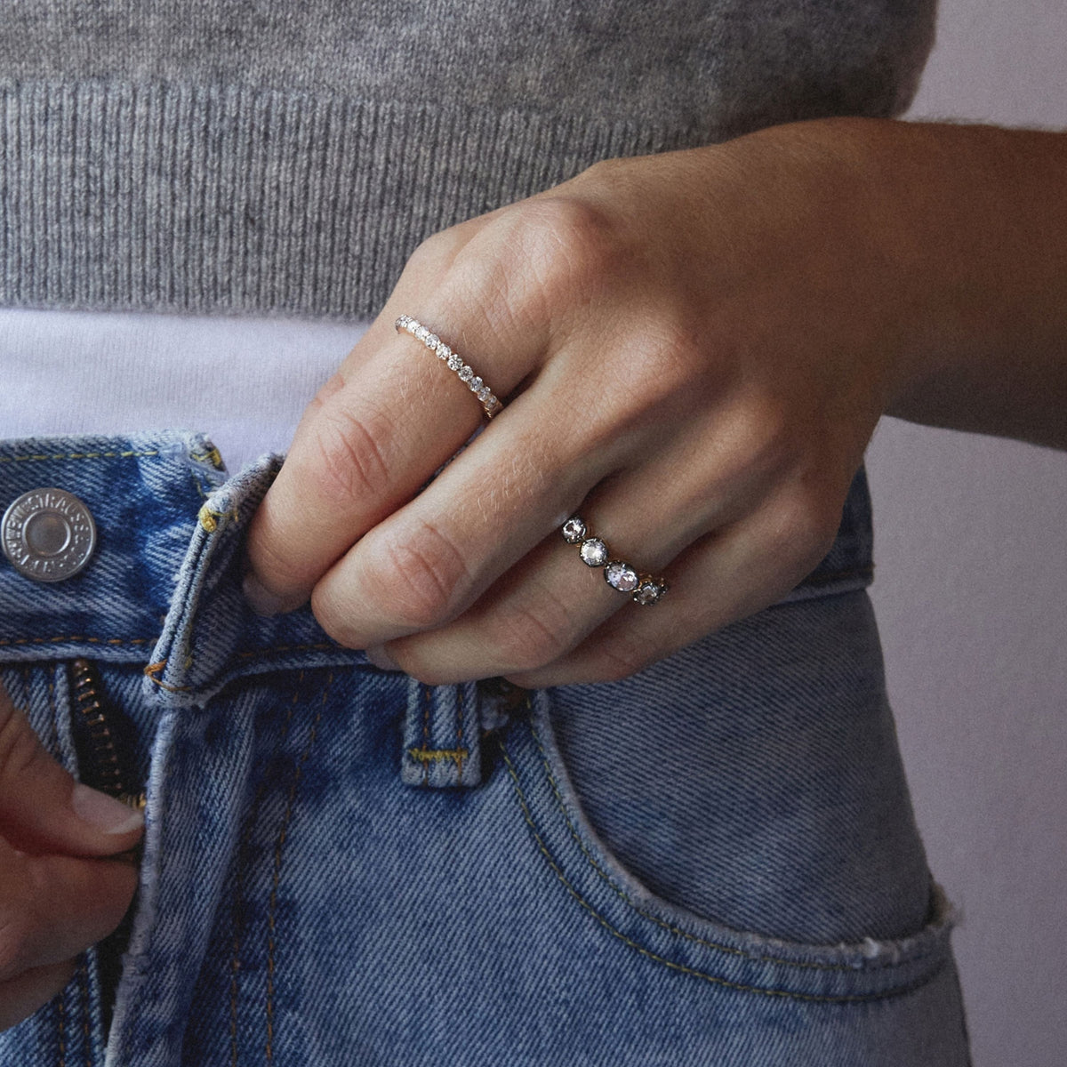 Model. Close up of a woman's hand unbuttoning her jeans with two gemstone rings. 