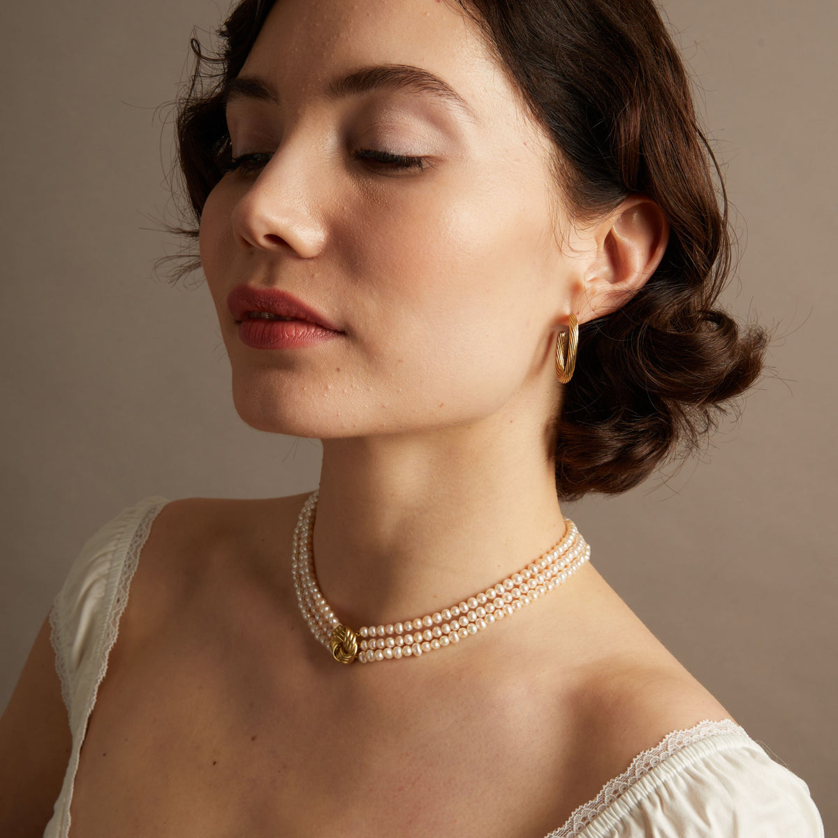 Woman wearing a pearl necklace and gold earrings against a neutral background
