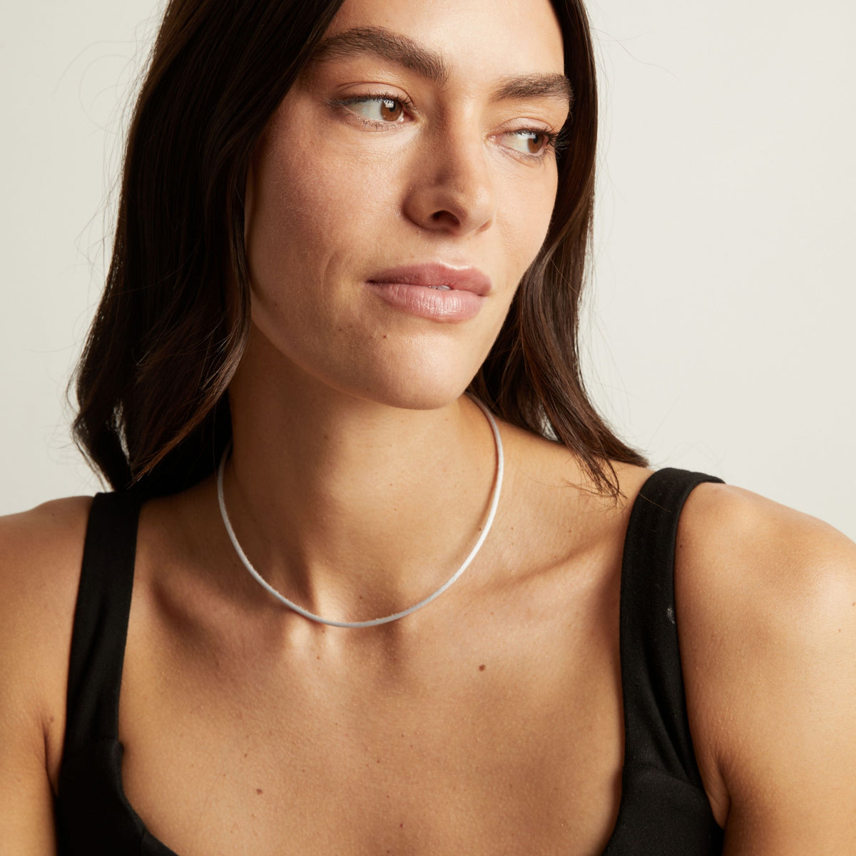 Model. A close-up of a model wearing a thin cord necklace, showing the necklace against her neck and upper chest.