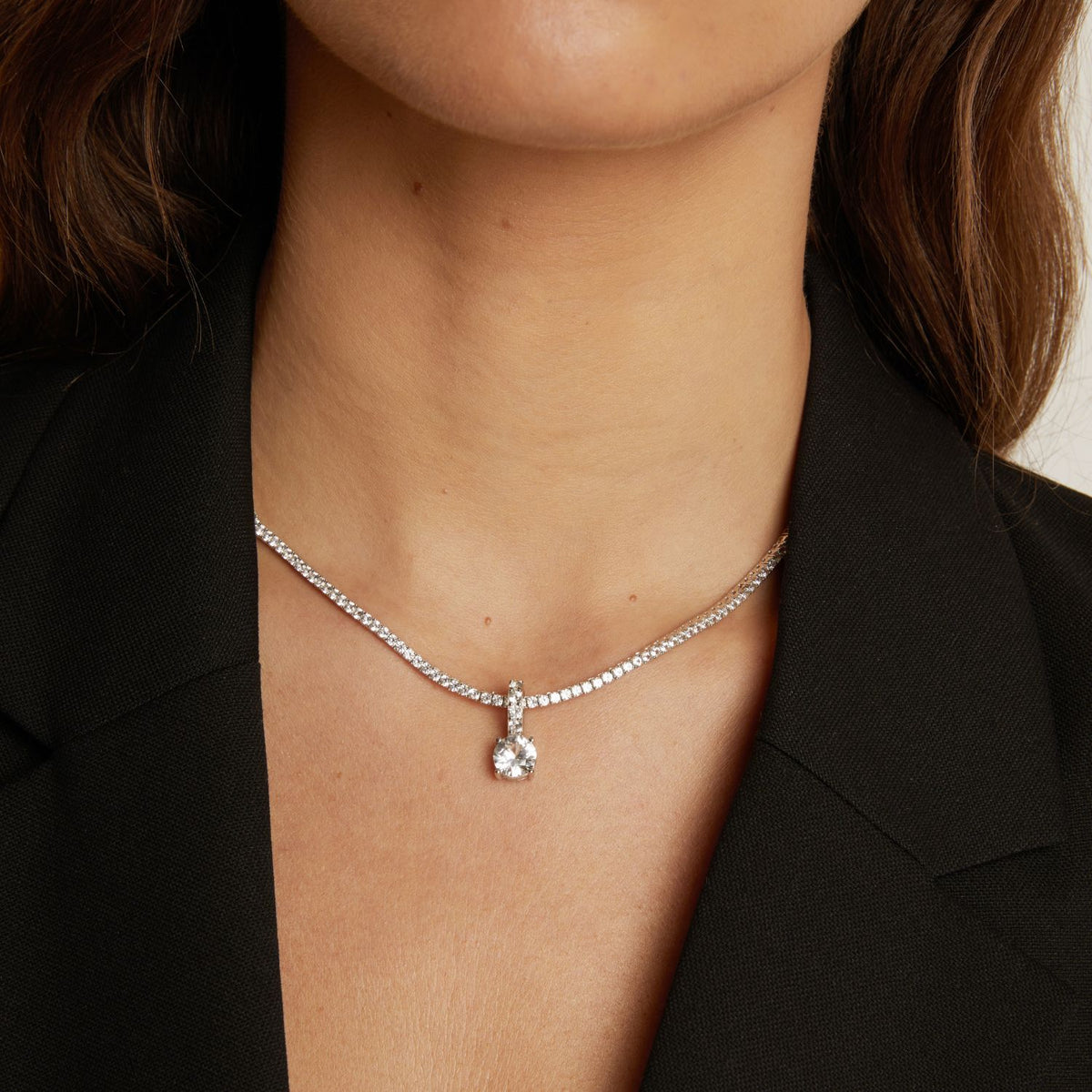 Model. Tennis necklace with a round gemstone pendant worn by a person against a neutral background.