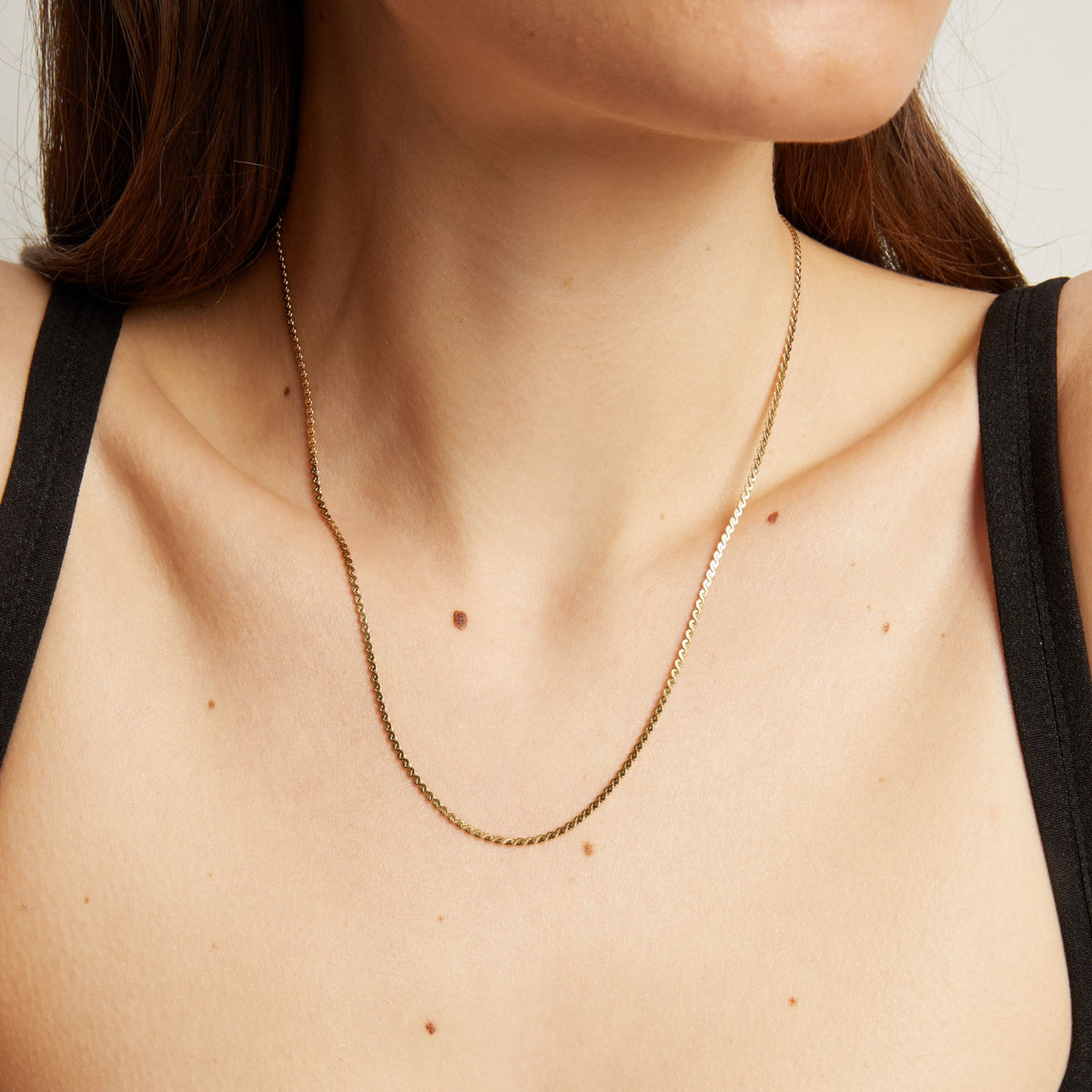 Gold necklace on a person wearing a black top against a neutral background.