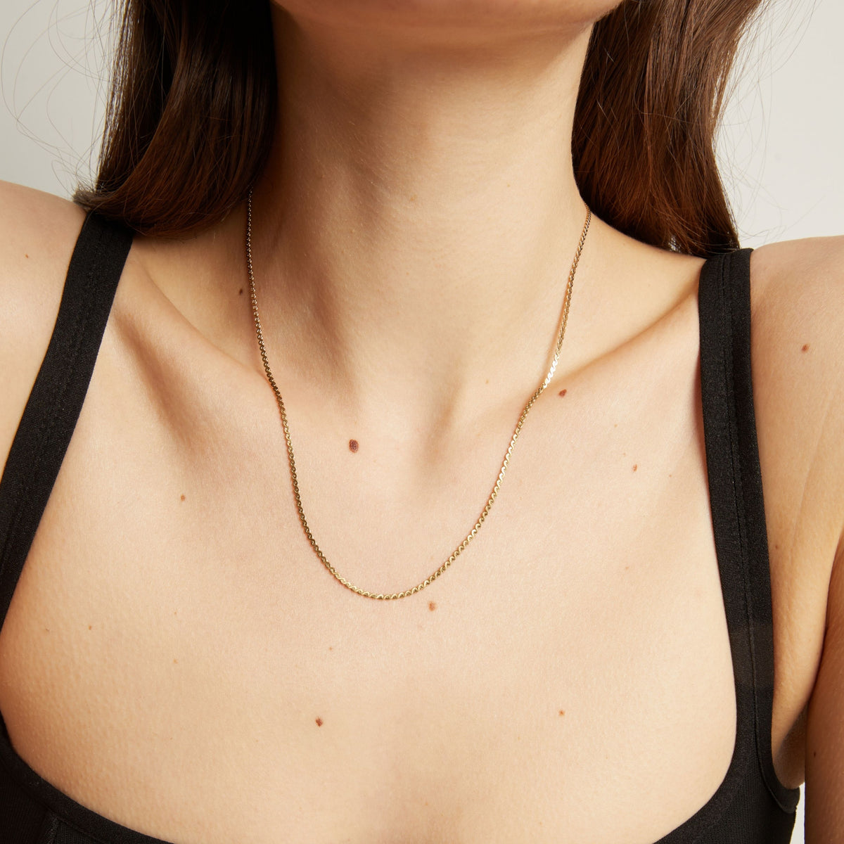 Gold necklace on a person wearing a black top against a neutral background.