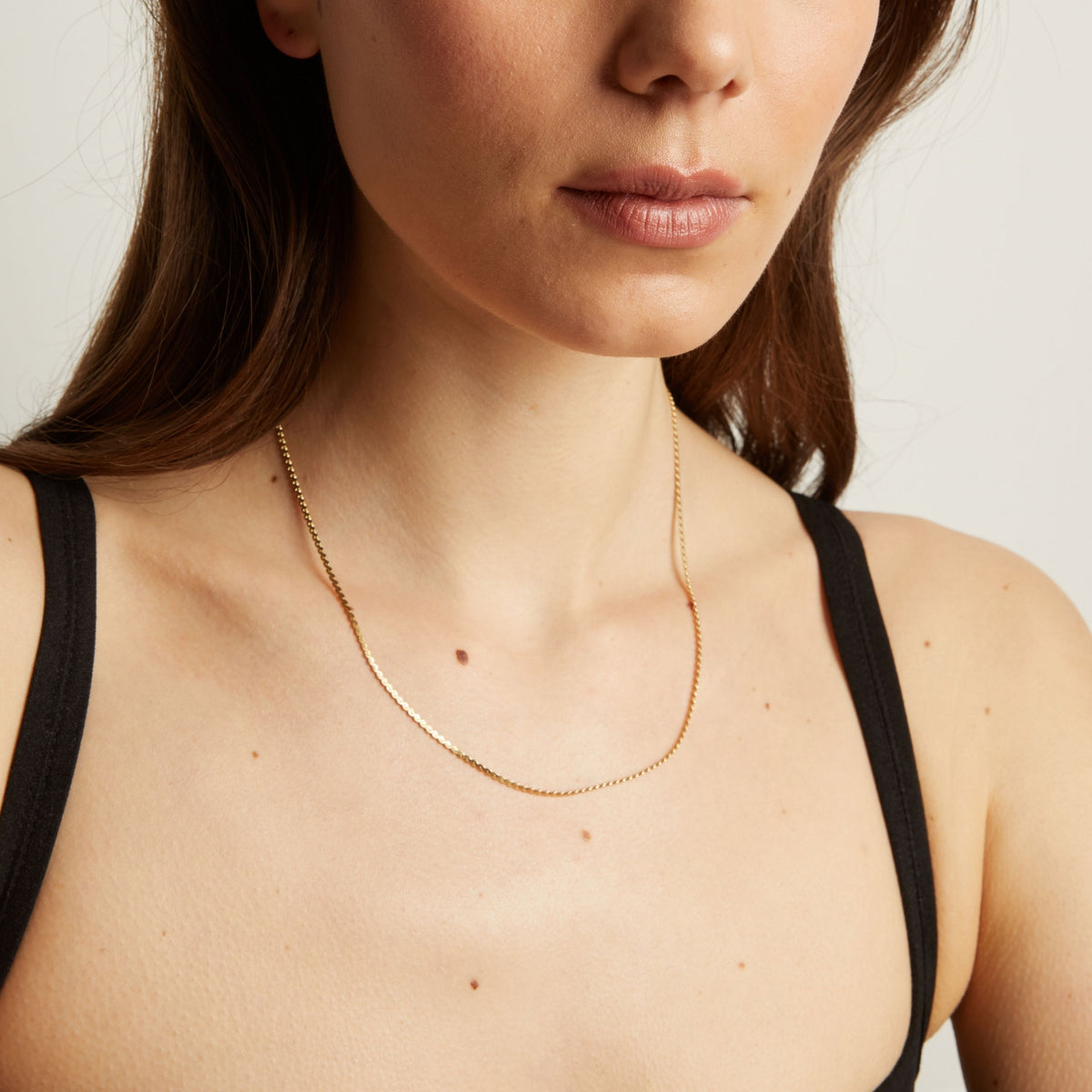 Gold necklace on a person wearing a black top against a neutral background.