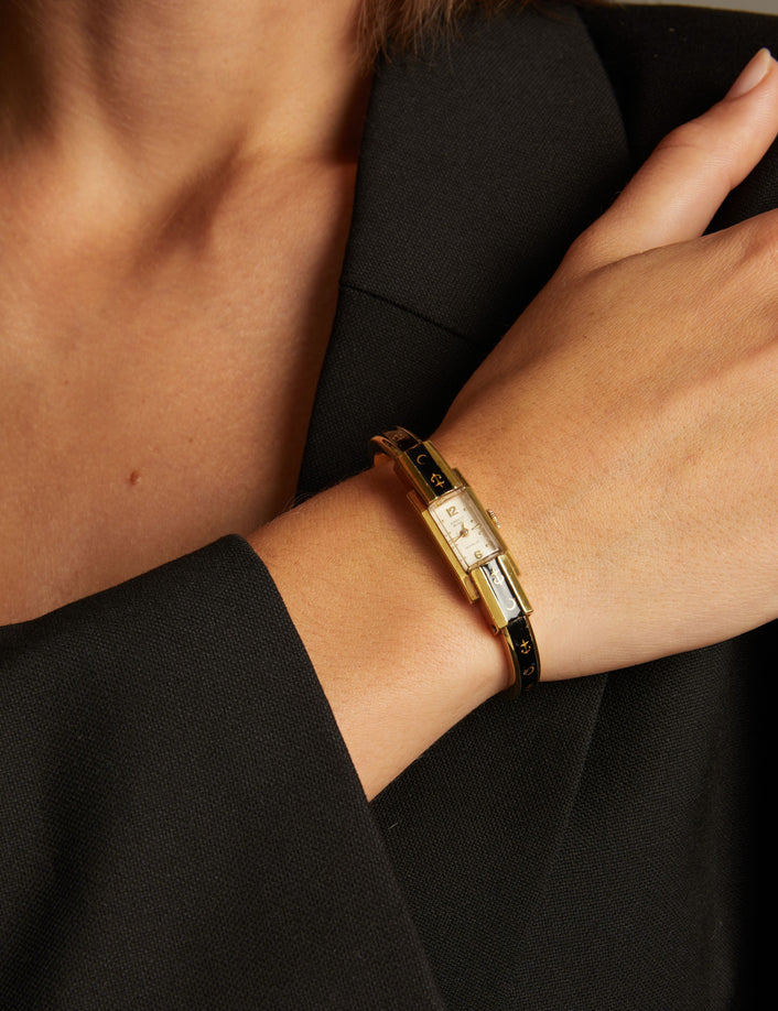 Model. Close up of a woman wearing a black and gold watch on neutral background.