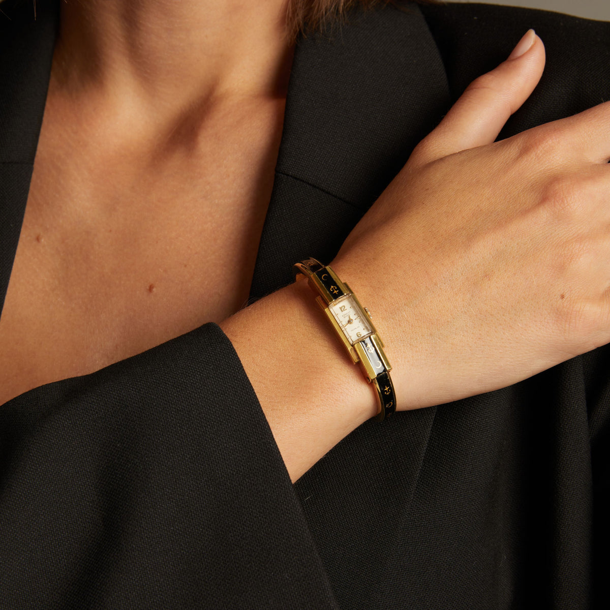 Model. Close up of a woman wearing a black and gold watch on neutral background.