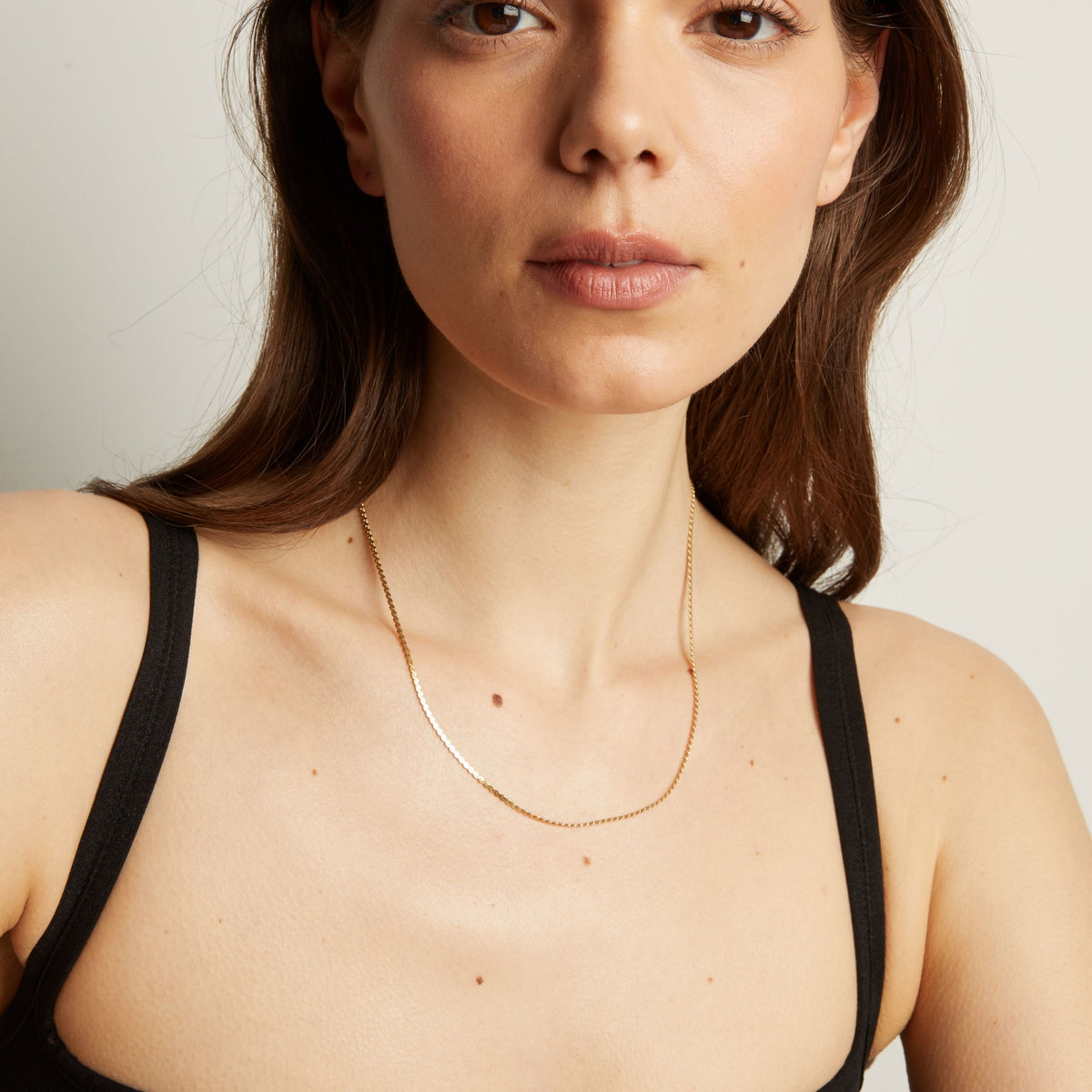 Gold necklace on a woman wearing a black top against a neutral background.