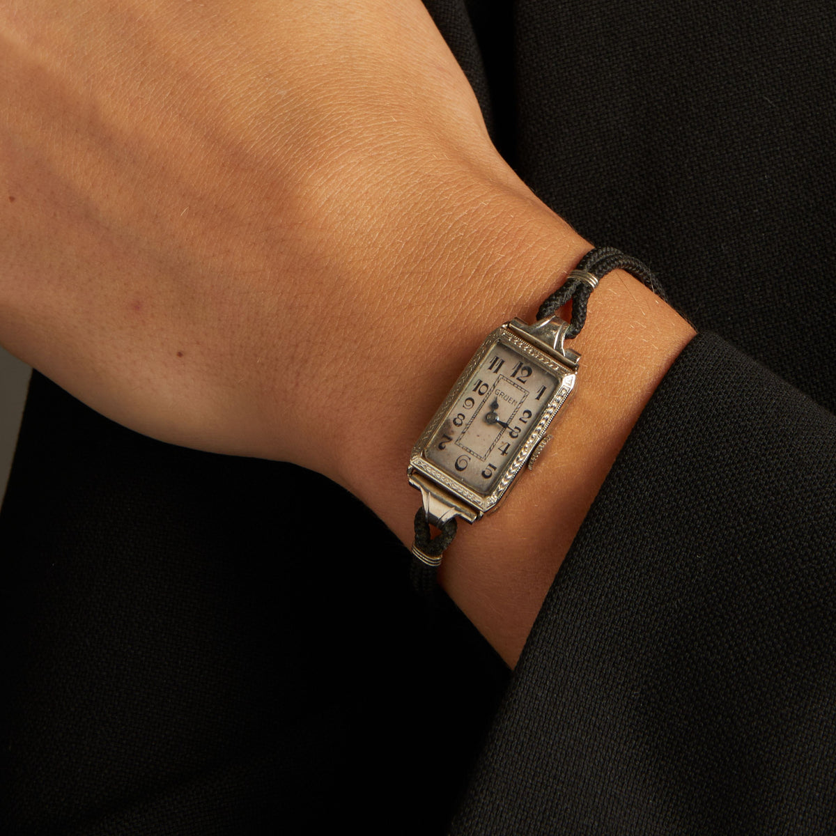 Model. Close up of a woman wearing a black rope watch with silver face on neutral background.