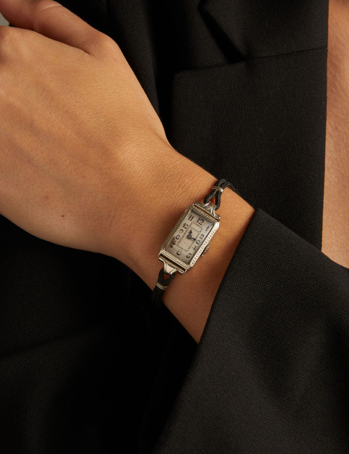 Model. Close up of a woman wearing a black rope watch with silver face on neutral background.