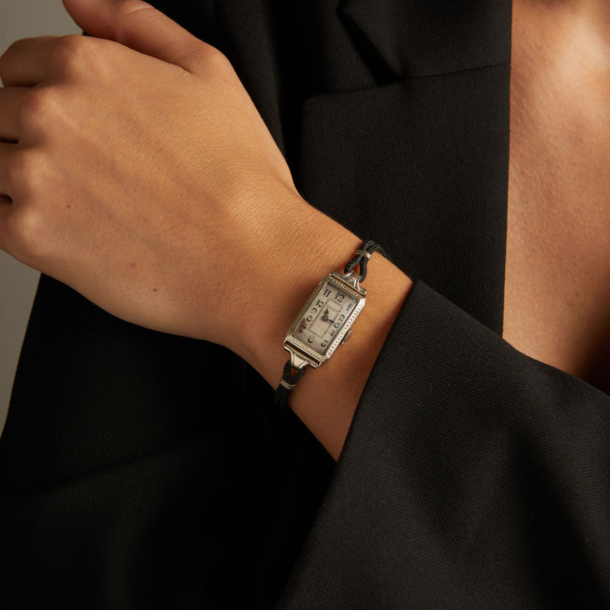 Model. Close up of a woman wearing a black rope watch with silver face on neutral background.