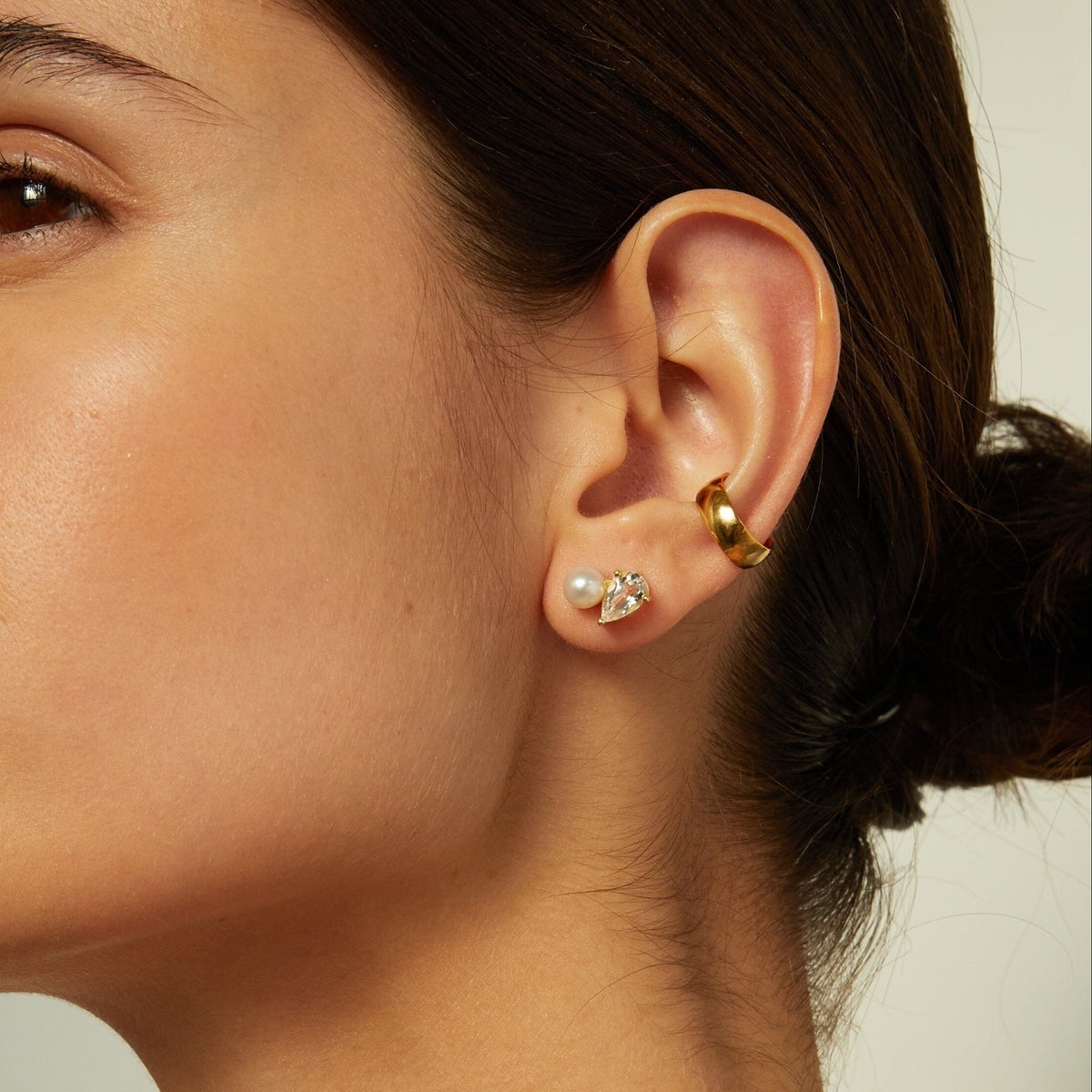 Model. Close-up of a woman's ear wearing pearl and gemstone stud earrings.