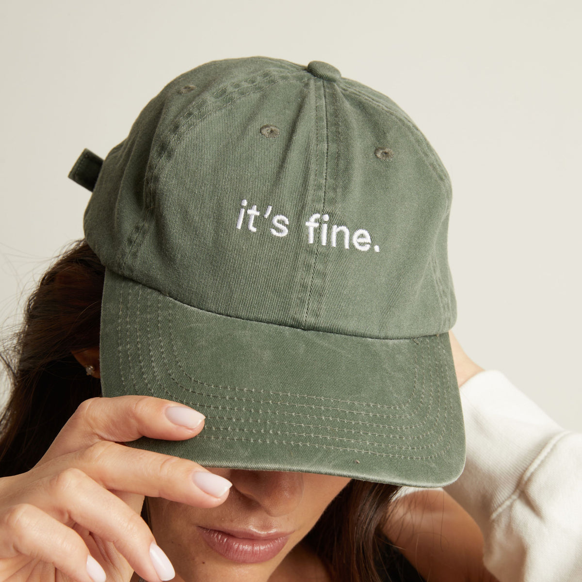 Woman wearing a green cap with 'it's fine' text on a plain background