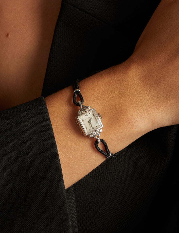 Model. Close up of a woman wearing a black rope watch with silver face with diamonds on neutral background.