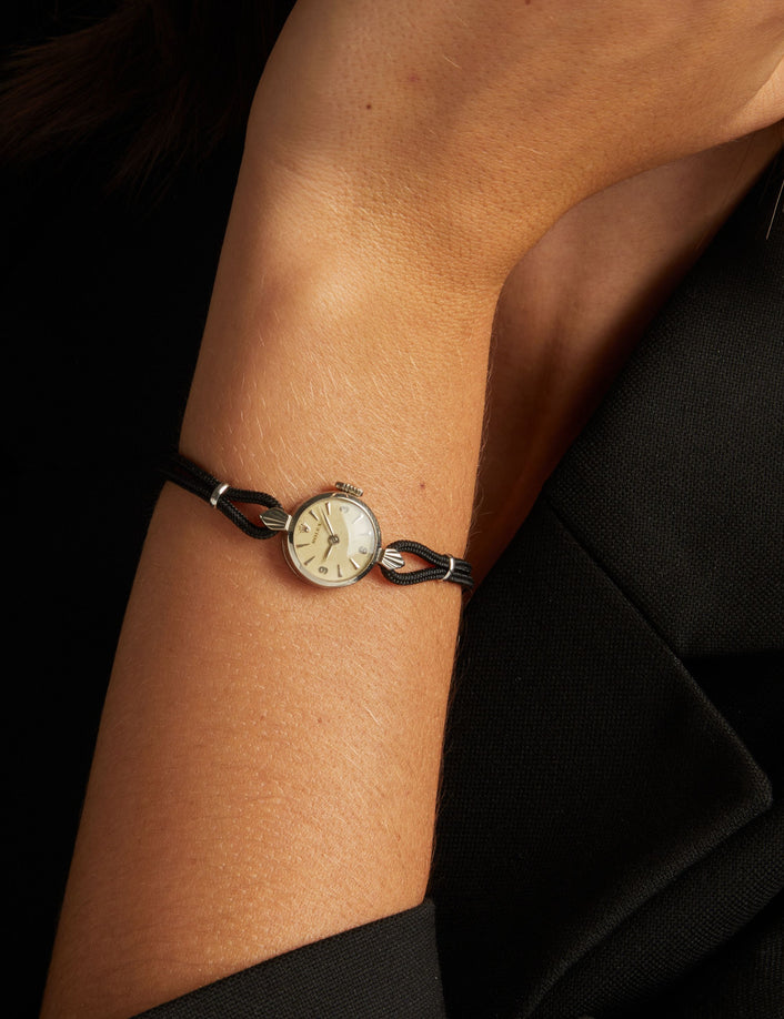 Model. Close up of a woman wearing a black rope watch with silver face on neutral background.