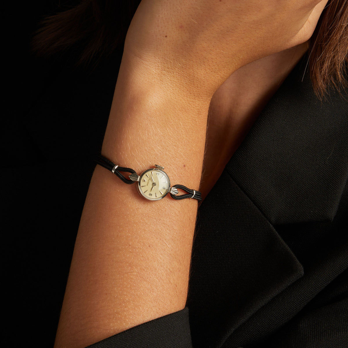 Model. Close up of a woman wearing a black rope watch with silver face on neutral background.