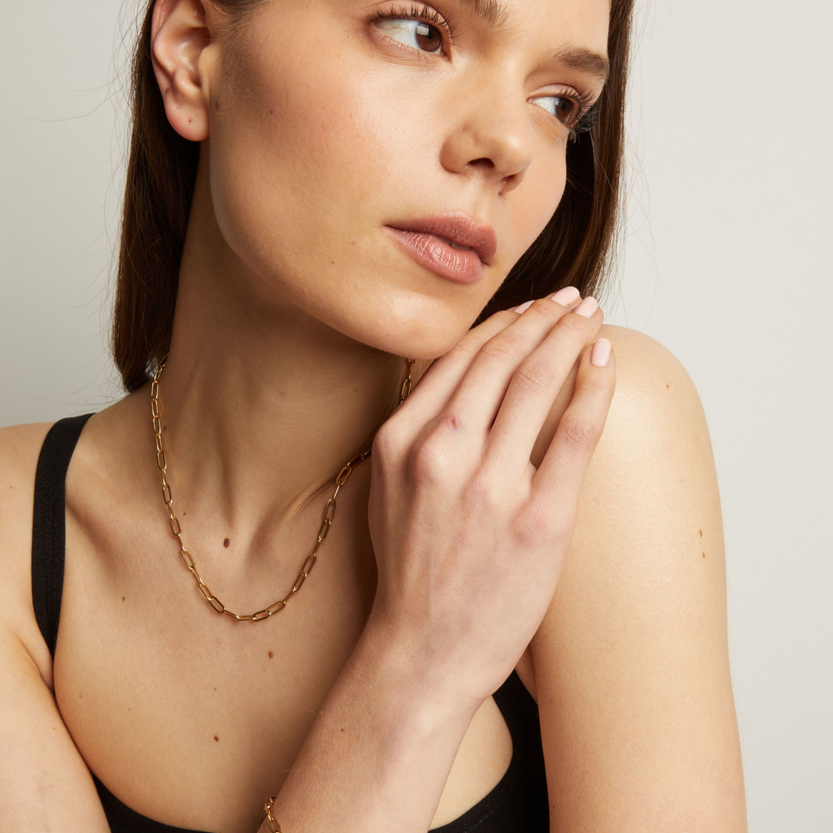 Woman wearing a gold necklace with a plain background.