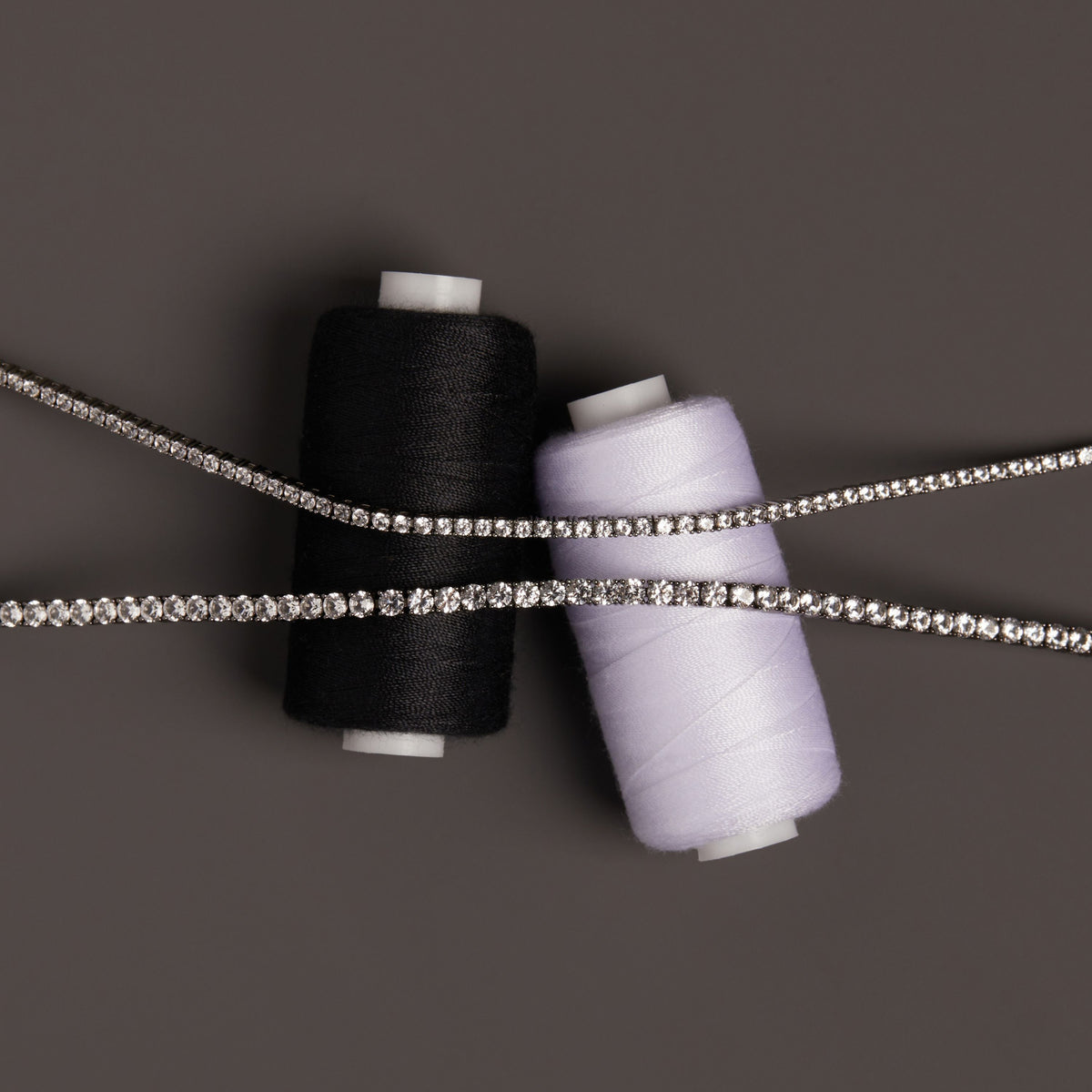 Model. Close up of two tennis bracelets on thread spools. 