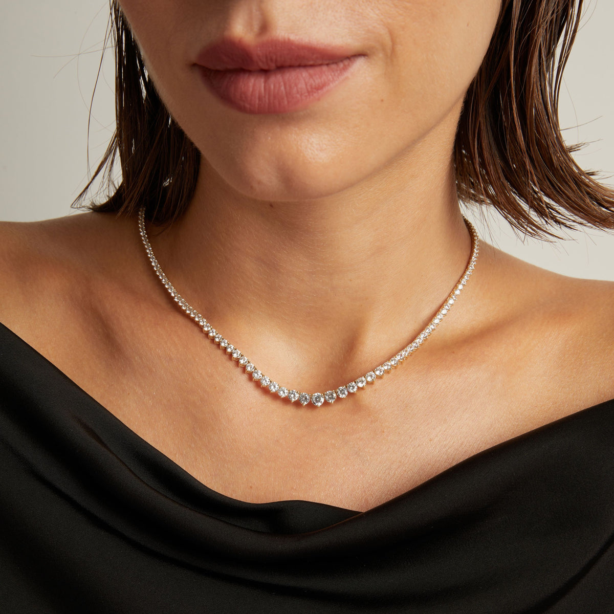 Model. Close up of a woman in a black top wearing a diamond tennis necklace on beige background.