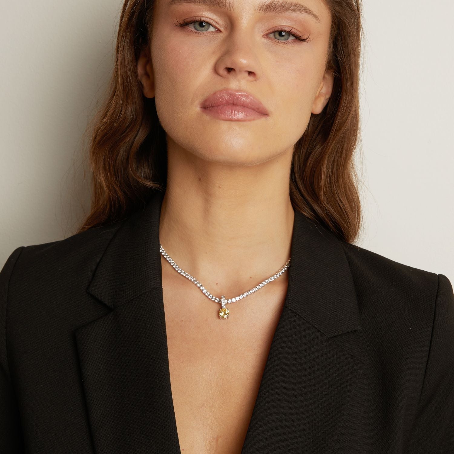 Model. Tennis necklace with a round gemstone pendant worn by a woman against a neutral background.