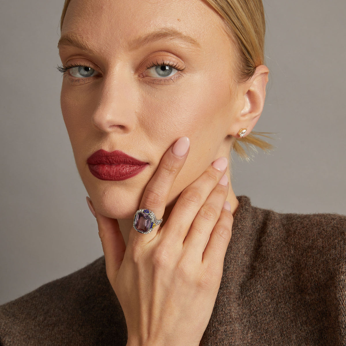 Model. Close up of woman wearing bold purple gemstone ring on neutral background.