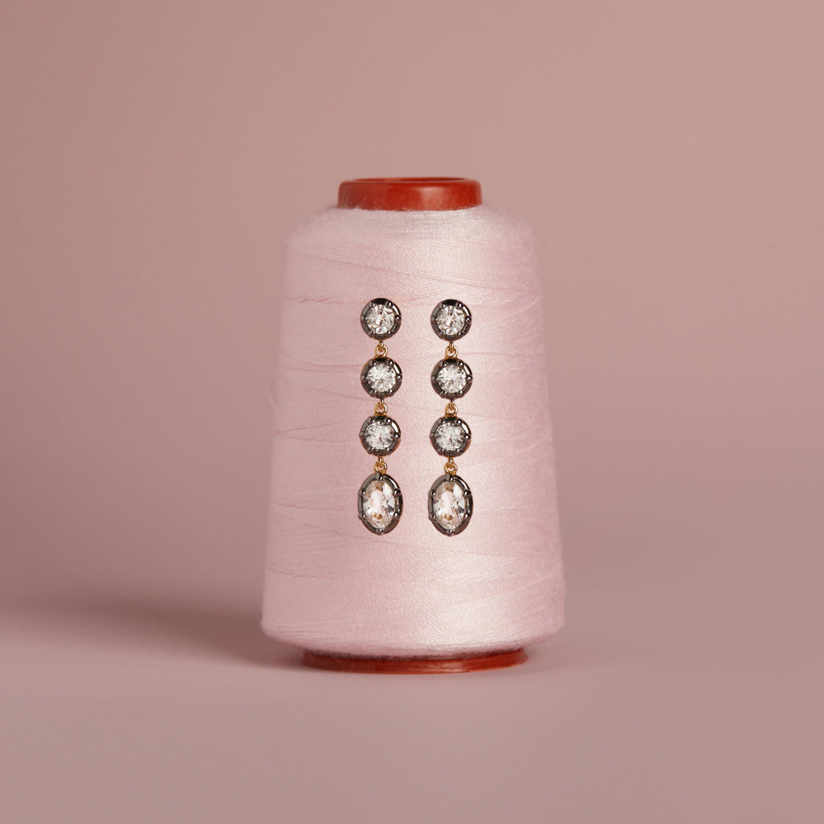 Model. Close up of gemstone tennis earrings on thread spool. 