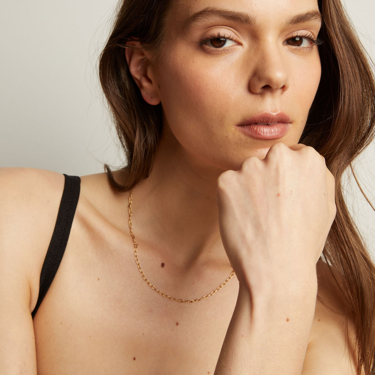 Gold necklace on a person with a neutral background.