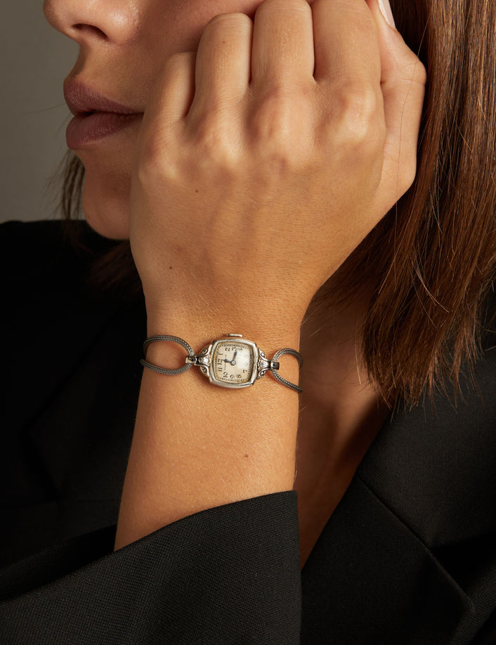 Model. Close up of a woman wearing a silver cord watch on a neutral background.