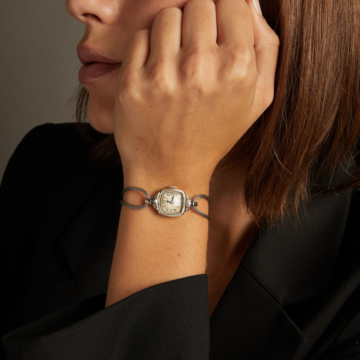 Model. Close up of a woman wearing a silver cord watch on a neutral background.