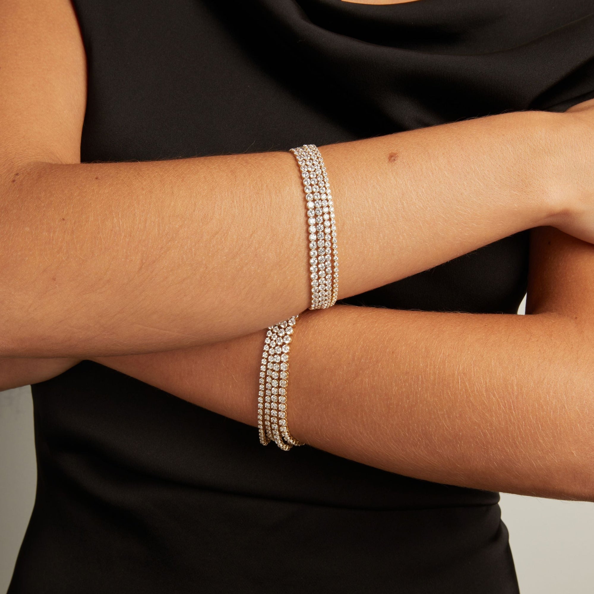 Model. Close up of a woman's crossed arms with stacked diamond tennis bracelets on both wrists.