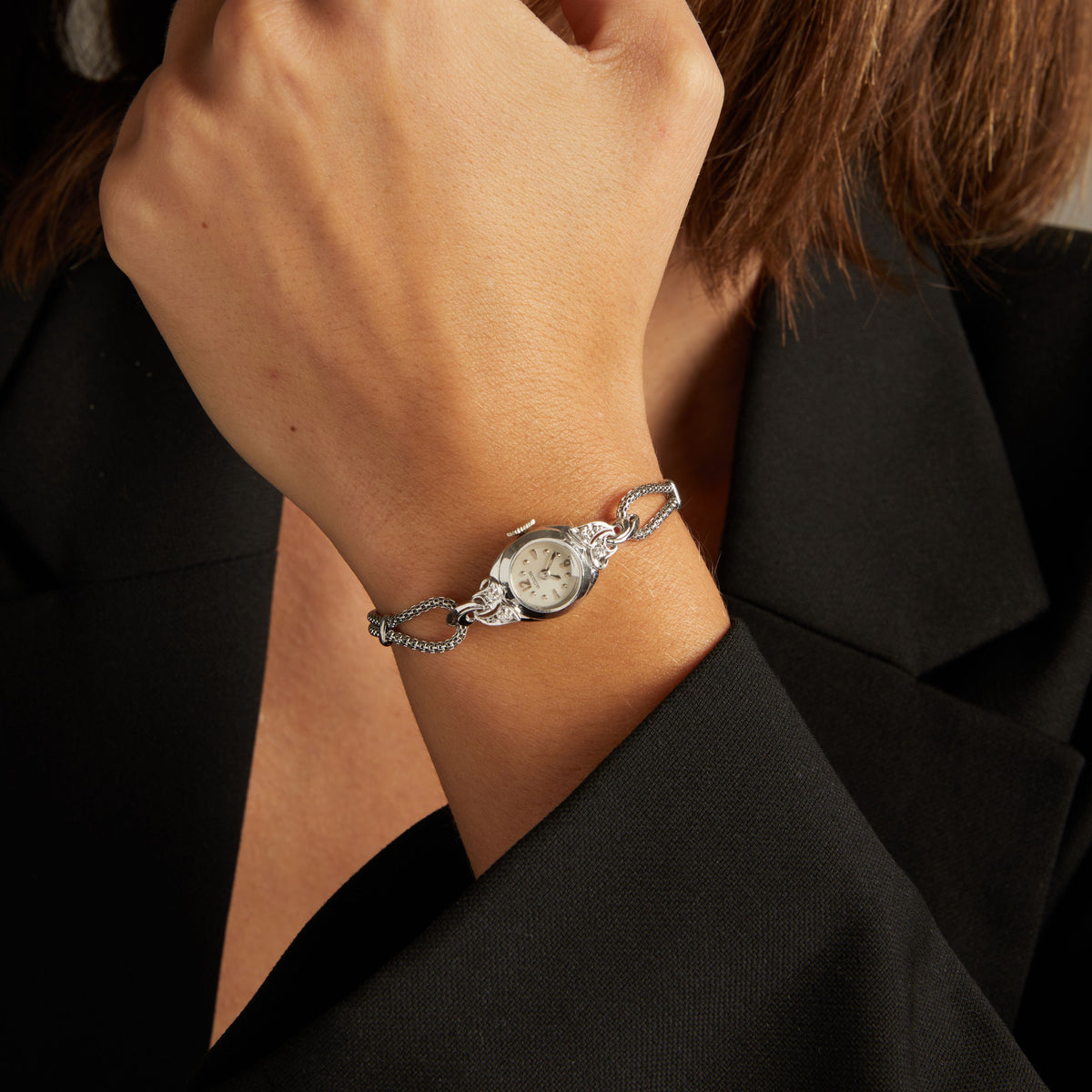Model. Close up of a woman wearing a silver chain watch on neutral background.
