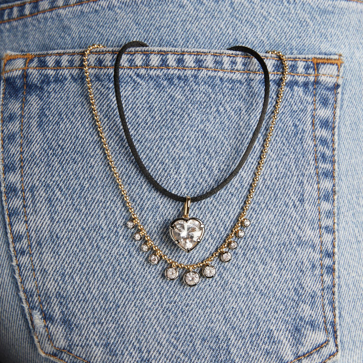 Model. Close up of two necklaces hanging out of denim pocket.