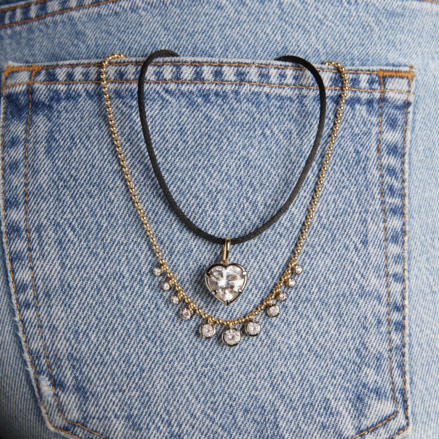 Model. Close up of two necklaces hanging out of denim pocket.