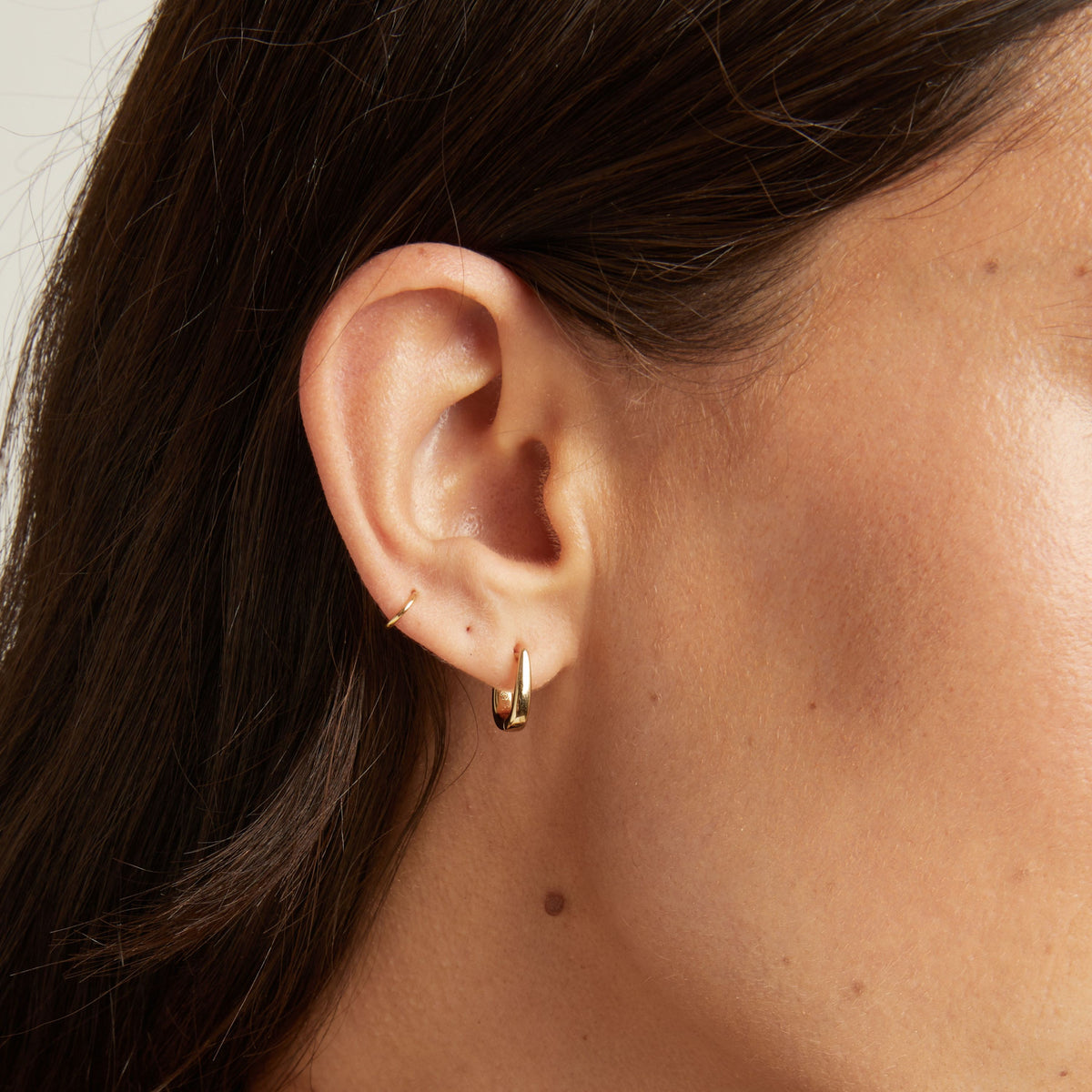 Model. Close up of woman's ear with gold huggie earring.