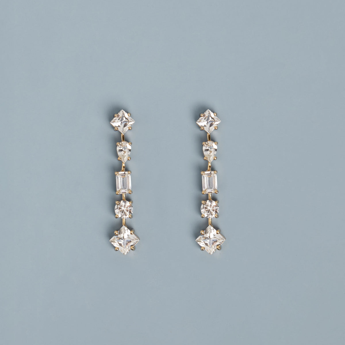 Model. Mixed gemstone tennis earrings on light blue background.