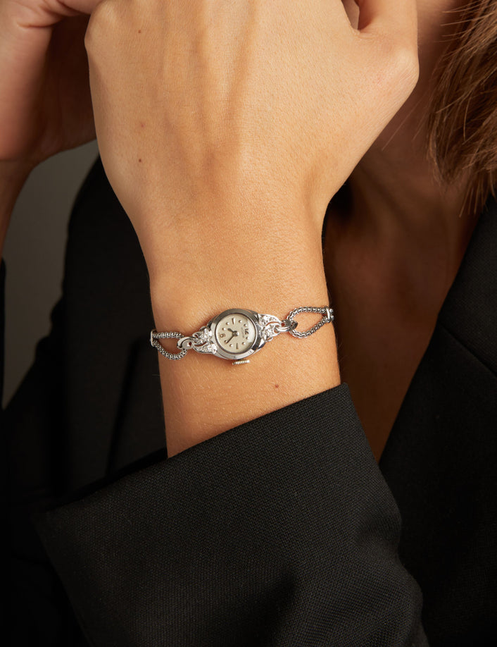 Model. Close up of a woman wearing a silver chain watch on neutral background.