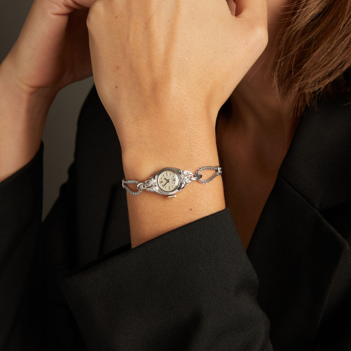 Model. Close up of a woman wearing a silver chain watch on neutral background.