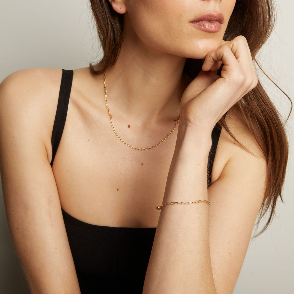 Woman wearing a delicate gold necklace and bracelet against a neutral background.