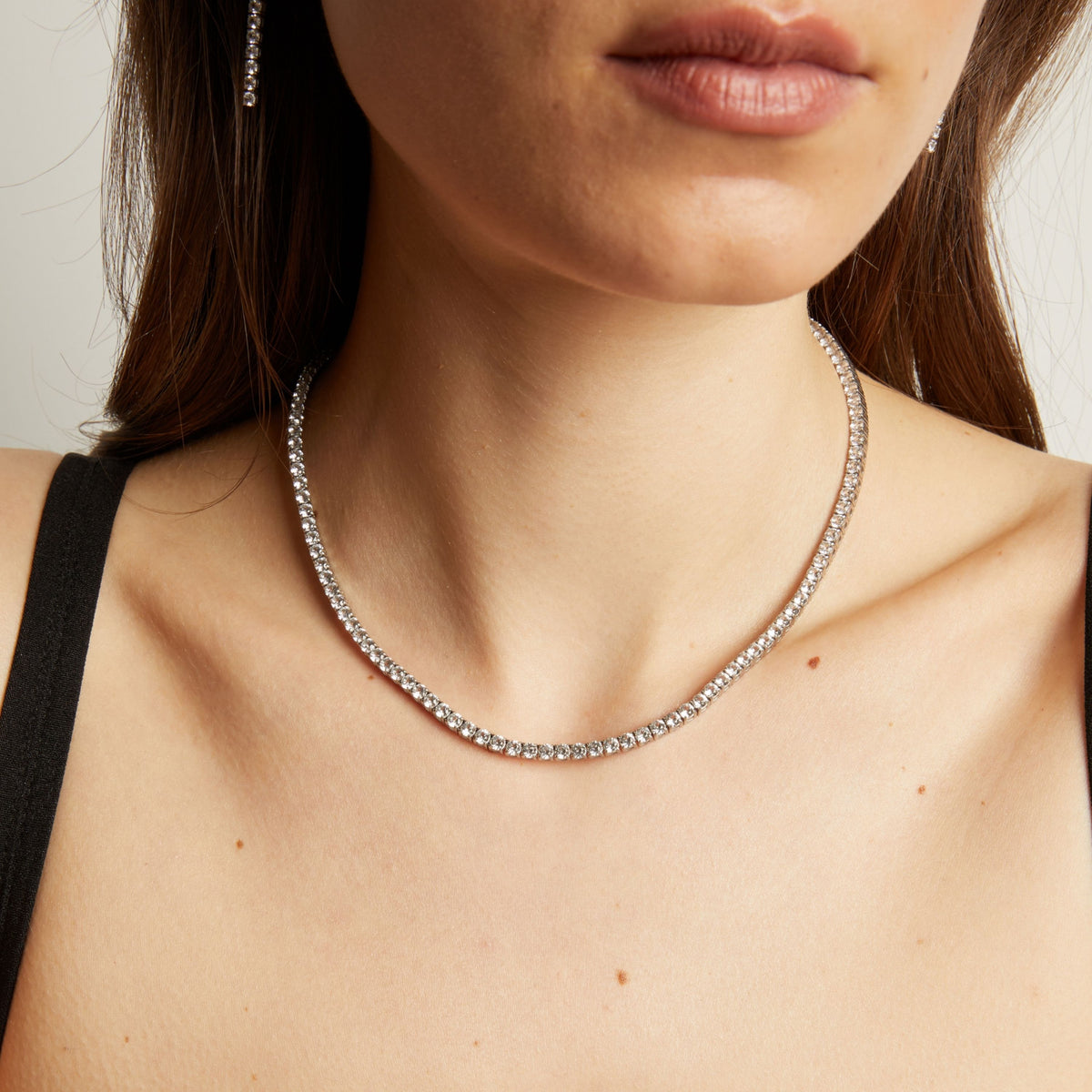 Close up of a woman wearing a tennis necklace against a neutral background.
