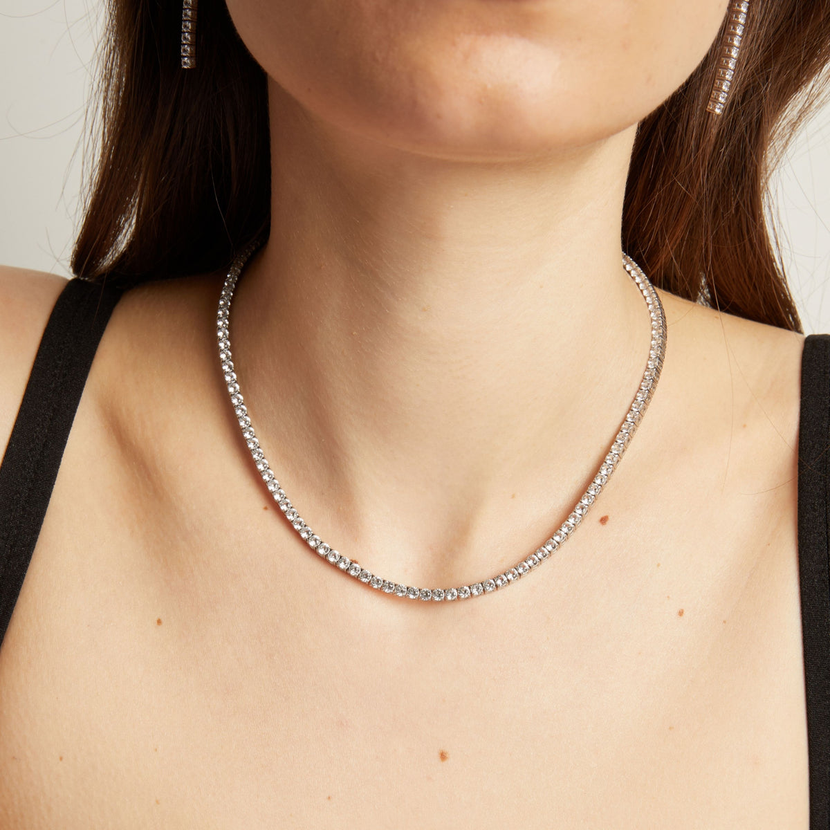 Close up of a woman wearing a tennis necklace against a neutral background.