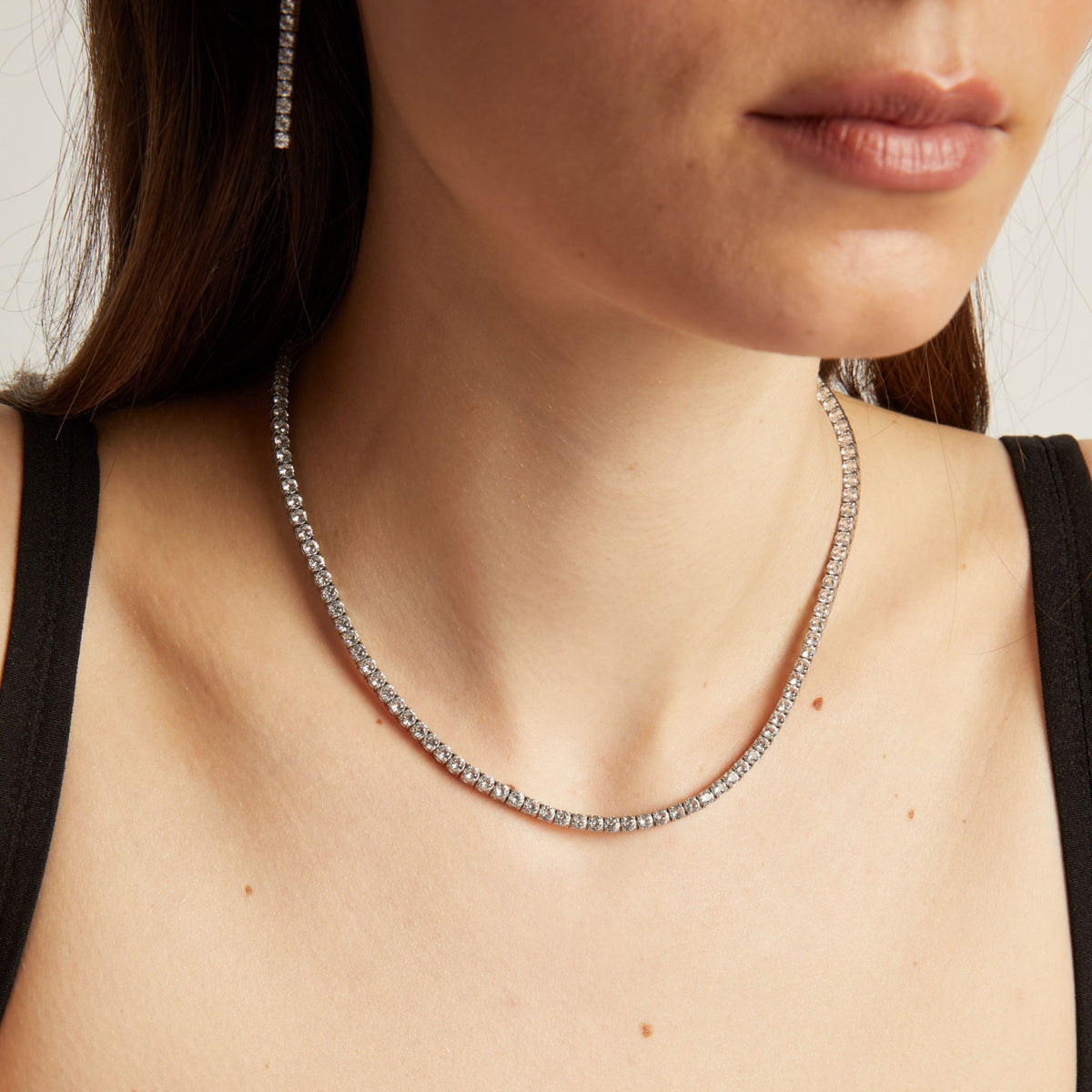 Close up of a woman wearing a tennis necklace against a neutral background.