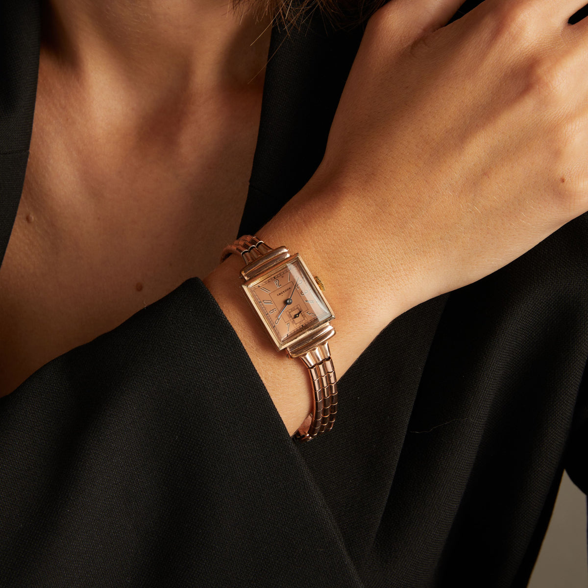 Model. Close up of a woman wearing a rose gold watch on neutral background.