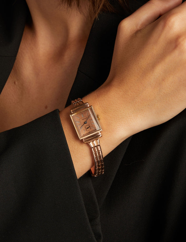 Model. Close up of a woman wearing a rose gold watch on neutral background.