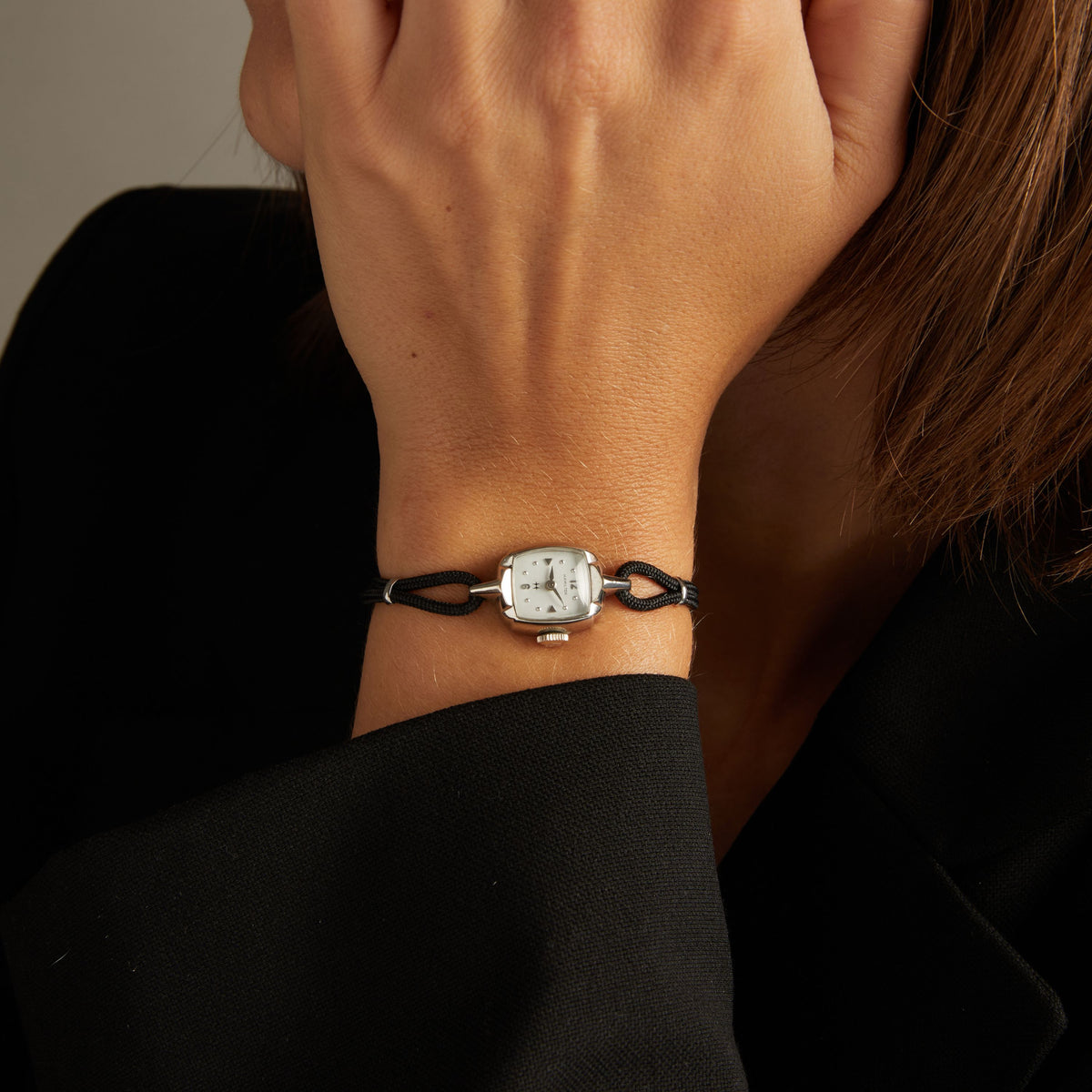 Model. Close up of a woman wearing a black rope watch with silver face on neutral background.