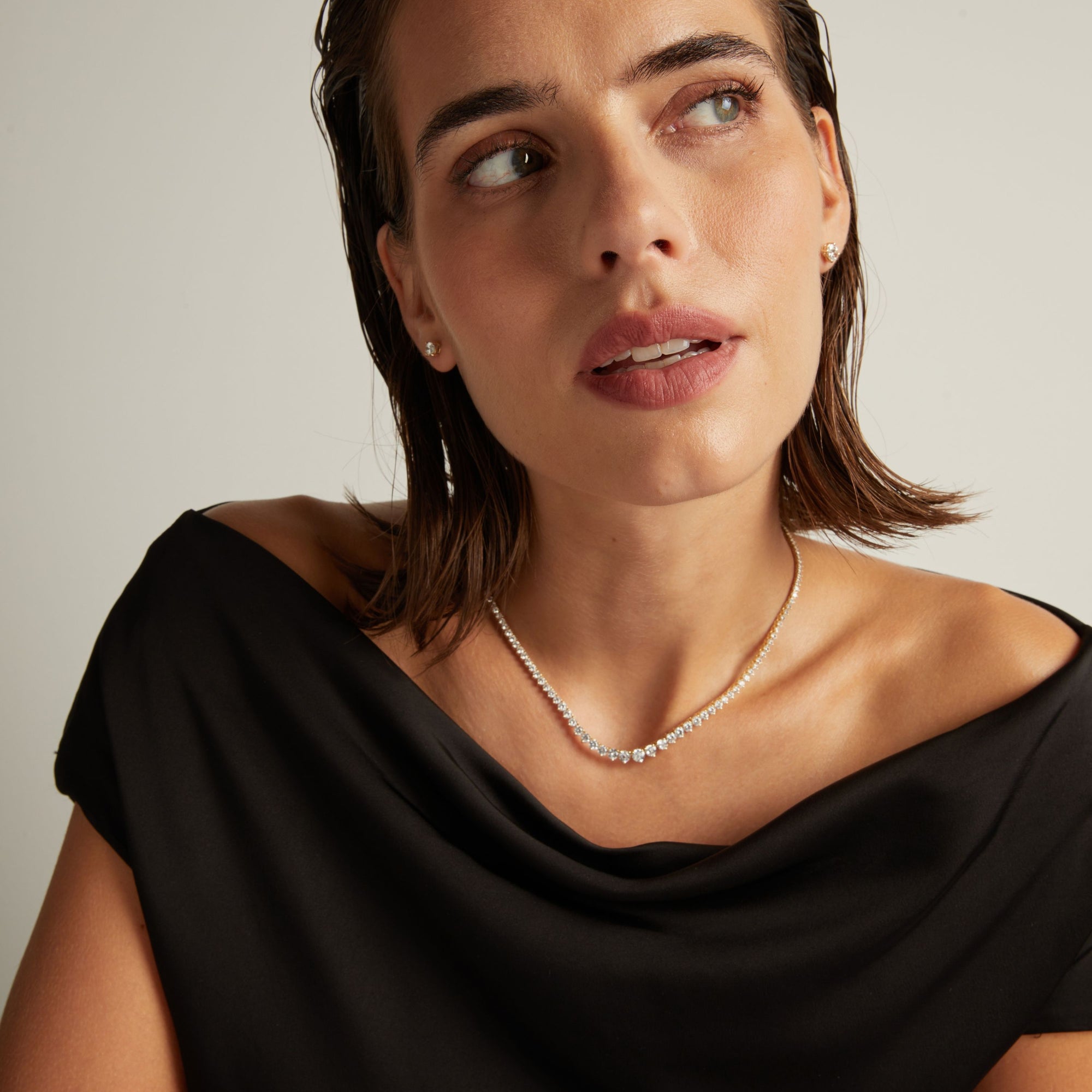 Model. Close up of a woman in a black top wearing a diamond tennis necklace on beige background.