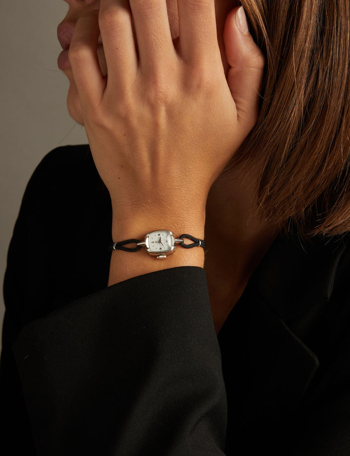 Model. Close up of a woman wearing a black rope watch with silver face on neutral background.