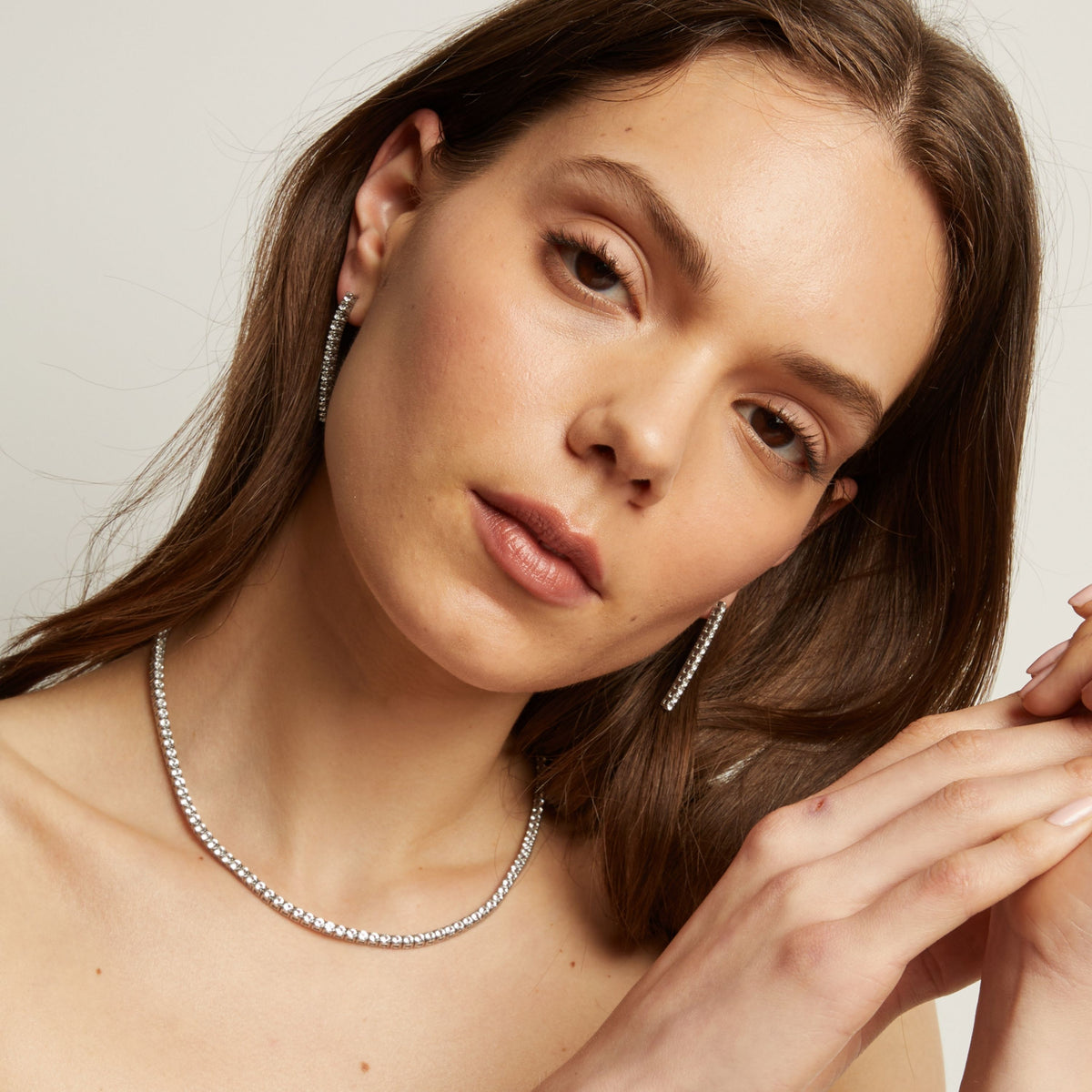A woman wearing tennis earrings and necklace with a neutral background.
