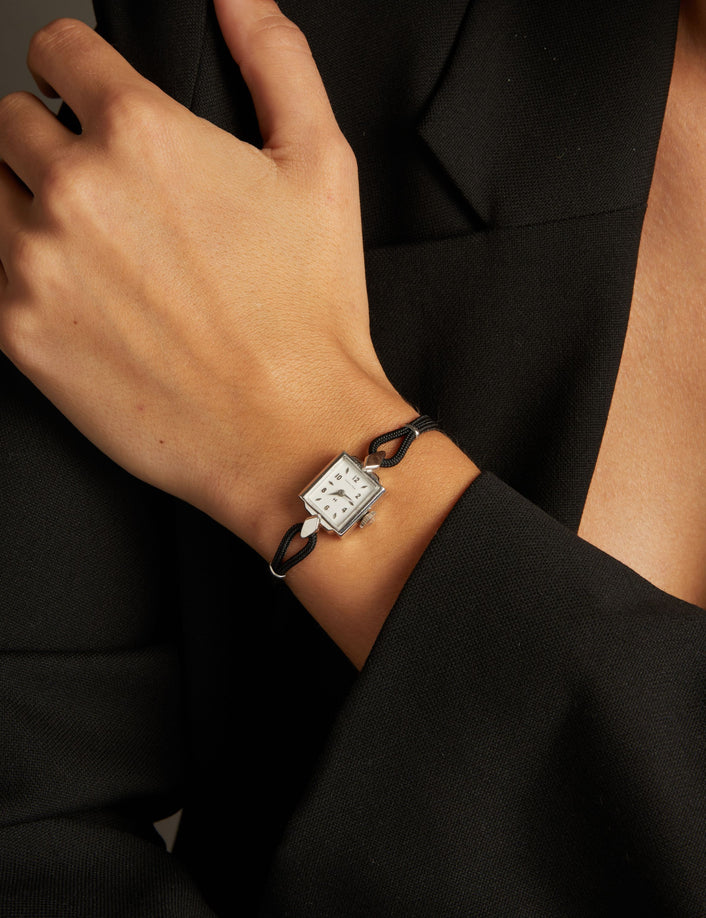 Model. Close up of a woman wearing a black rope watch with silver face on neutral background.