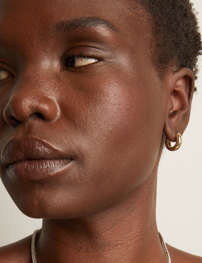 Model. Close-up of a person wearing a gold hoop earring against a neutral background