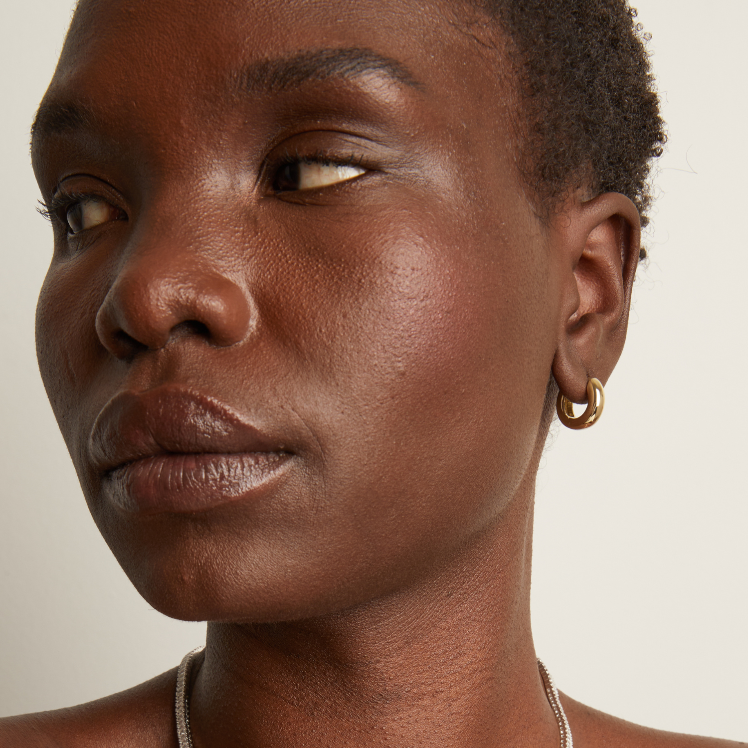 Model. Close-up of a person wearing a gold hoop earring against a neutral background