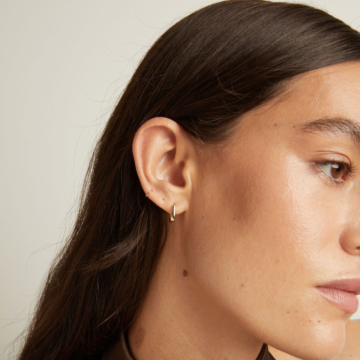 Model. Close up of woman wearing gold huggie earring.